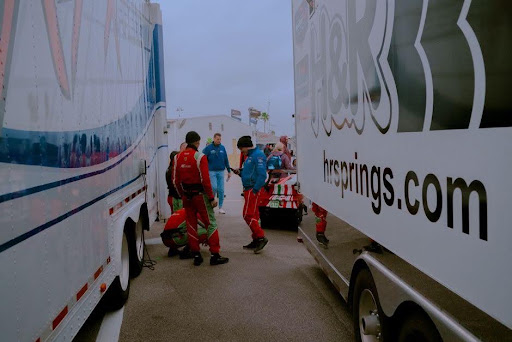 Race Haulers and the Miles Between Tracks Race team in red uniforms preparing cars amidst trailers on race day.