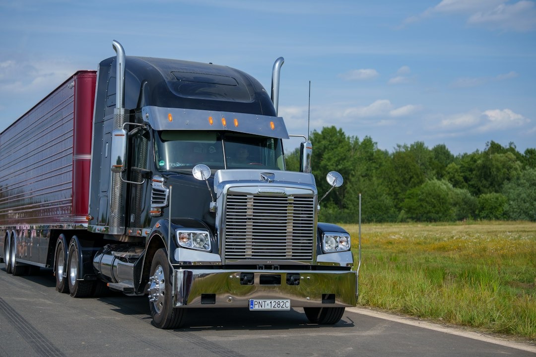A black semi-truck drives down a rural road